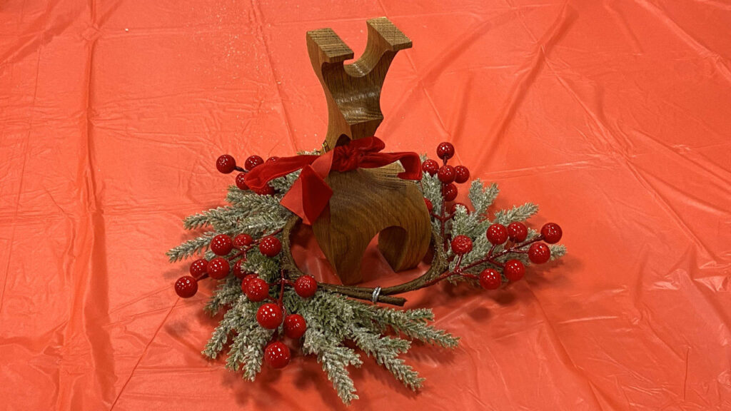 A stylized wooden reindeer wrapped in a holly branch decoration.