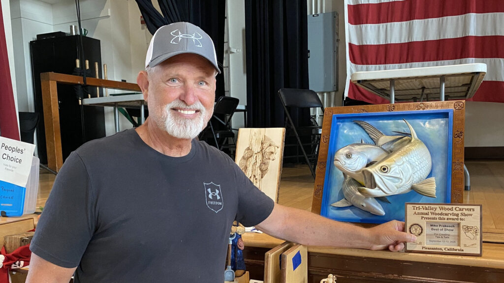 Mike Prokosch holds his Best of Show award plaque next to his silver fish wood relief carving at the 2026 Tri-Valley Carvers Show in Pleasanton, California.